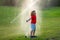 Child play in summer garden. Grass watering. Automatic sprinkler irrigation system in a green park watering lawn