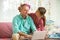 Child playing and disturbing father working remotely from home. Little girl combing daddy's hair. Man on couch with laptop.