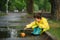 Child playing with toy boat in puddle. Kid play outdoor by rain. Fall rainy weather outdoors activity for young children. Kid