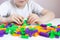 A child plays with a bright constructor on a white table. The development of fine motor skills of the hands. Quarantined home