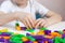 A child plays with a bright constructor on a white table. Hands of a child with a toy close-up. Home leisure for children