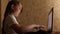 Child plays on computer in evening in the room. young girl does her homework on laptop. girl types in search query on a