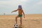 The child plays football on the beach.