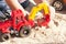 A child plays in the sand with big toy cars, an excavator, a truck