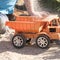 A child plays in the sand with big toy cars, an excavator, a truck