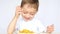 A child with pleasure eating potato chips sitting at a table on a white background. The boy is eating chips and smiling.