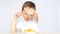 A child with pleasure eating potato chips sitting at a table on a white background. The boy shows the thumb of his hand