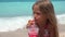 Child portrait drinking juice on beach, thirsty girl face view on seashore 4K