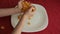 Child pours corn flakes in a white plate on a red tablecloth