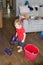 A child puts the house in order with a vacuum cleaner in one hand and a bucket of water and a rag to wash the floor in the other.