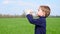 The child quenches thirst, drinks water from a transparent plastic bottle, standing on a green lawn, in slow motion