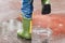 Child with rain boots jumps into a puddle