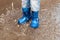 Child with rain boots jumps into a puddle.