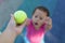 Child reaches for tennis ball from teacher