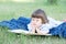 Child reading book lying on stomach outdoor, smiling cute little girl, children education and development