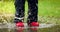 Child with red rubber boots jump in rain puddle. waterproof clothing