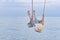 Child riding on rope swing over the water and lifted high legs. Vacation at sea