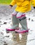 A child in rubber boots jumps in a puddle