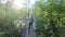 The child runs along the path and reaches the hanging wooden bridge over the river