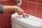 Child`s hand finger presses button on the water draining into the toilet bowl, close-up