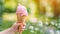 Child s hand grasping pink ice cream in waffle cone at green park, summer sweetness