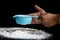 The child`s hand is holding sifted flour to sift the white powder on a black background.