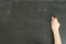 Child`s hand holding white chalk on black chalkboard background