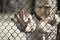 The child`s hands are holding onto a metal mesh fence. The problem of forced deportation of Ukrainian children from the