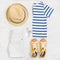 Child`s striped t-shirt, demin shorts, accessories, yellow shoes and straw hat isolated on white background. Top view
