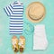 Child`s striped t-shirt, denim shorts, accessories, yellow shoes and straw hat on turquoise wooden background. Top view