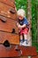 Child in safety harness climb high in adventure rope park