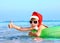 Child in santa hat floating on inflatable ring in sea.