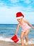 Child in santa hat playing on beach.