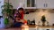 Child in a Santa hat is sitting in a festive kitchen decorated for Christmas. Happy girl catches a gift box and funny grimaces.