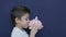 Child savings concept. Caucasian boy playing with his piggy bank with funny face expressions. Isolated on blue