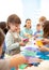 Child with scissors in hands cutting paper with teacher in class room. Group of children doing project in kindergarten