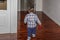 A child seen from behind is walking in the living room of his house, while carrying a wallet in his hand
