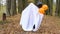 A child in sheets with cutout for eyes like a ghost costume dancing in an autumn forest scares and terrifies. A kind little funny