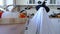 A child in sheets with cutout for eyes like a ghost costume in the kitchen decorated for the Halloween holiday. A kind little