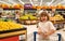 Child with shopping cart full of fresh organic vegetables and fruits standing in grocery department of food store or