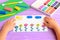 Child shows a card with plasticine flowers, sun and clouds. Supplies for children art crafts on wooden table. Modeling clay craft