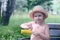 The child sits on a bench and holds a corn in her hands. Beautiful smiling girl in a straw hat.