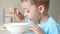 The child sits at the kitchen table, eating soup with a spoon from a white plate.