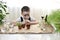 The child sits with a magnifying glass in front of his face with his eyes closed in front of pot growing plants