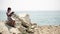 A child sits on a stone near the Adriatic Sea and draws a picture.