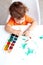 A child sits at a table and draws green watercolors paints. Baby art. Vertical photo