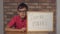 Child sitting at the desk holding flipchart with lettering fired on the background red brick wall.