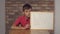 Child sitting at the desk holding flipchart with lettering nop on the background red brick wall.