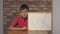 Child sitting at the desk holding flipchart with lettering ok on the background red brick wall.