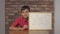 Child sitting at the desk holding flipchart with lettering yea on the background red brick wall.